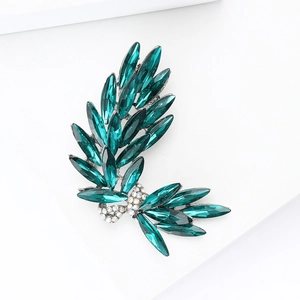 Macro detail of emerald marquise cut gems and silver bow brooch in a leaf pattern