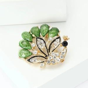 Elegant gold peacock brooch with green gemstones and sparkling rhinestones on white base