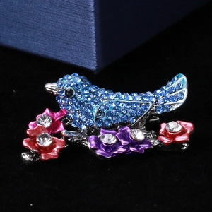 Detailed close-up of blue rhinestone bird brooch with colorful flowers on black velvet