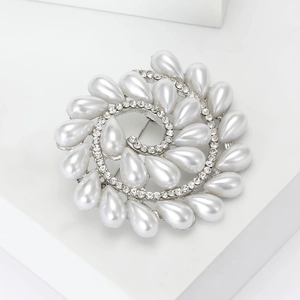 Elegante broche en espiral con perlas blancas y diamantes de imitación en un pedestal