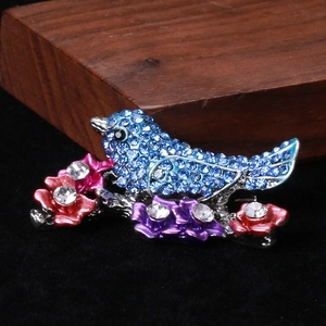 Macro detail of bird brooch featuring blue rhinestones and pink enamel floral accents