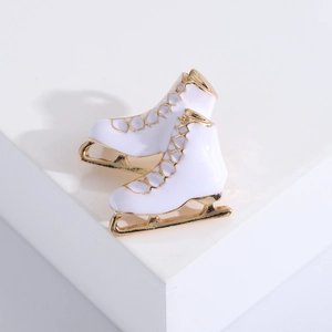 Detalle de broches de patines de hielo en esmalte blanco y dorado sobre bloque blanco