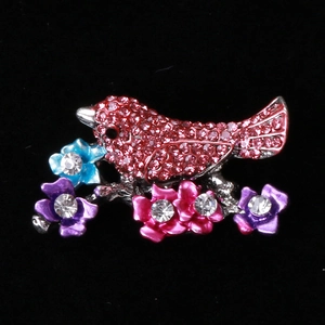 Detail of bird brooch with red rhinestones and colorful floral accents on silver metal
