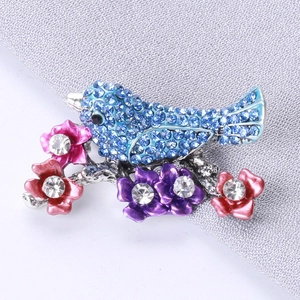Close-up of blue rhinestone bird brooch with pink and purple flowers on silver alloy branch