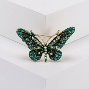 Elegant vintage gold-plated butterfly brooch with green rhinestones on geometric display