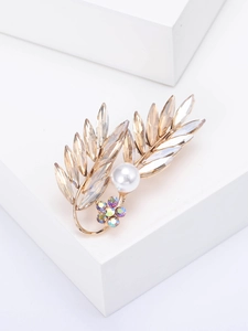 Détail d'une broche fleur dorée avec cristaux champagne et une perle blanche centrale