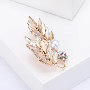Détail de la broche feuille en cristal doré avec perle blanche et strass multicolores