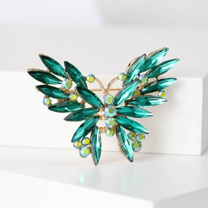 Macro detail of butterfly brooch featuring green marquise crystals and gold-tone alloy
