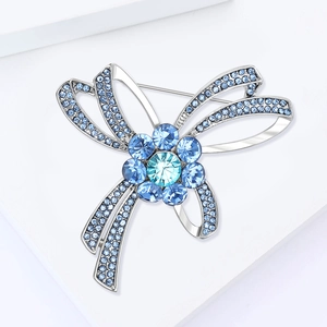 Détail de la broche nœud argentée avec des strass bleus et un motif floral central