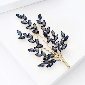 Detailed macro view of golden leaf brooch with navy blue marquise crystals