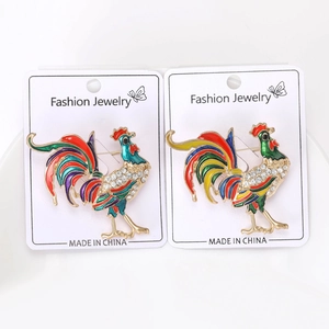 Dettaglio di spille a gallo in smalto colorato con cristalli su carta per gioielli