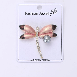 Macro detail of dragonfly brooch with pink gradient wings, rhinestones, and grey pearl