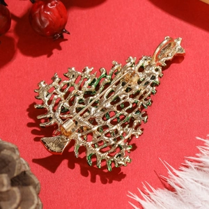 Golden Christmas tree brooch with green enamel and safety pin clasp on red festive background