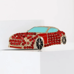 Detail of a red rhinestone car brooch with gold base on a white geometric prop