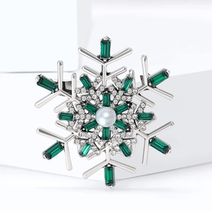Close-up of snowflake brooch with emerald stones and pearl on white geometric background