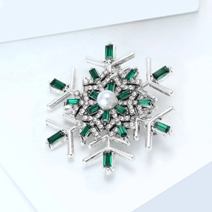Macro view of snowflake brooch featuring green emerald-cut stones and a white center pearl