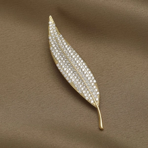 Macro shot of gold leaf brooch with white zircons on brown satin background fabric