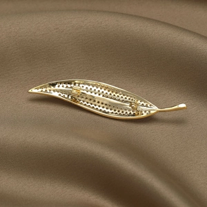 Leaf shaped golden brooch pin back view with detailed metal craft on silk background