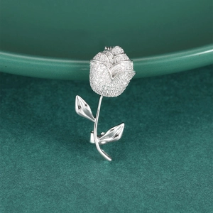 Elegant silver rose brooch with white cubic zirconia crystals on dark green tray