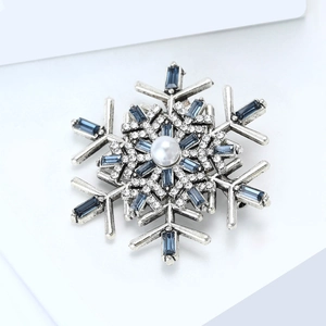 Detail of silver snowflake brooch featuring blue gems, a white pearl, and clear crystals