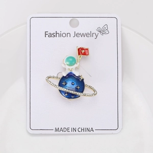 Dettaglio della spilla creativa con astronauta e pianeta blu con strass su carta