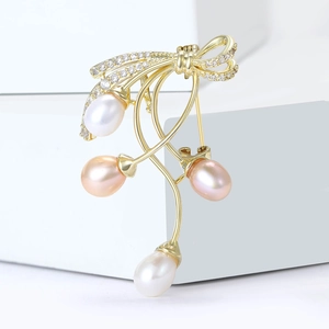 Elegant bow-shaped brooch with inlaid rhinestones and hanging freshwater pearls on white pedestal