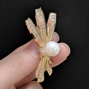 Détail d'une broche nœud dorée ornée de zircons brillants et d'une perle ronde blanche