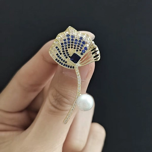Macro detail of leaf brooch with blue zircons, square stone and pearl accents