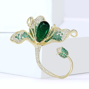 Détail d'une broche magnolia dorée avec pierre verte en poire et zircons brillants