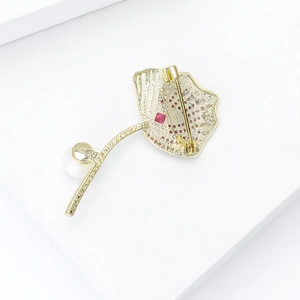 Back view of gold leaf brooch with micro-pave zircons and white pearl on white background