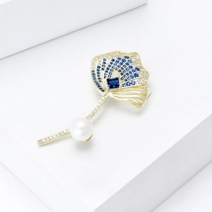 Detail of leaf brooch with blue zircon inlay and white round pearl on white pedestal