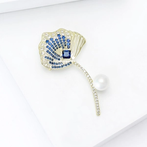 Macro detail of leaf brooch with blue zircons, golden finish, and white pearl
