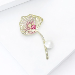 Macro detail of leaf brooch with pink cubic zirconia, red gemstone, and white pearl