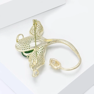 Vue détaillée de la broche léopard dorée avec cristaux verts sur un socle blanc