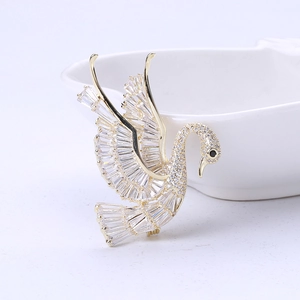 Close-up of golden swan brooch with baguette and round zircon crystals on ceramic