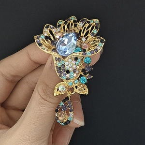 Macro detail of floral brooch showing gold filigree, blue gems and colorful rhinestones