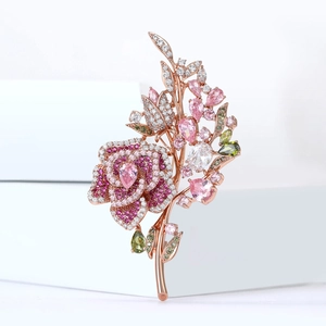 Macro detail of rose gold flower brooch with pink zircons and green marquise stones