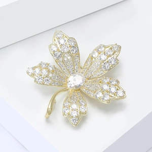 Elegant gold maple leaf brooch with sparkling zircons on a white minimalist pedestal