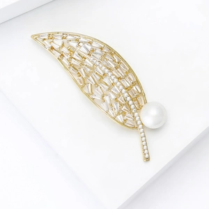 Détail d'une broche feuille dorée avec zircons brillants et perle blanche sur socle blanc