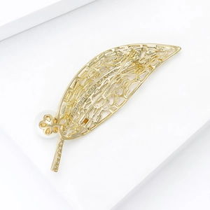 Broche élégante en forme de feuille dorée avec zircons et perles sur fond blanc épuré