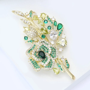 Detailed macro view of gold-plated rose brooch with micro-set green and clear zircons