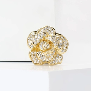 Elegant gold flower brooch with sparkling cubic zirconia on a white geometric stand