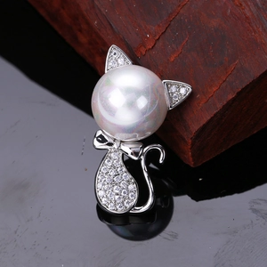 Close-up of a silver cat brooch with micro-paved zircons and a large pearl on wood