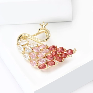 Élégante broche cygne dorée avec cristaux rouges et roses sur un piédestal blanc