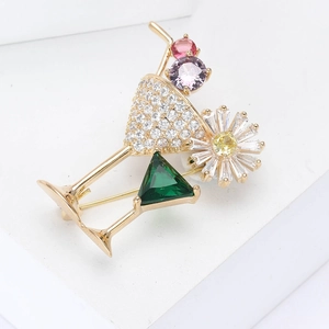 Broche cocktail élégante avec pierre émeraude et détail marguerite sur support blanc