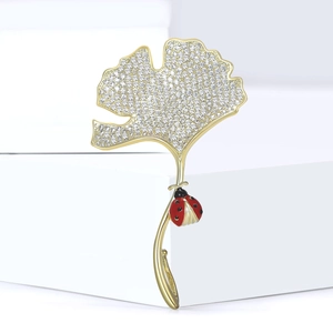Elegante goudkleurige ginkgoblad broche met zirkonia en rode lieveheersbeestje detail