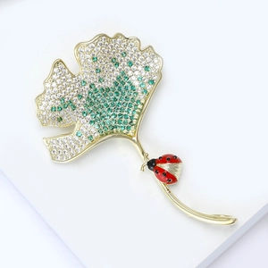 Detail van een vergulde ginkgo blad broche met groene zirkonia en een klein lieveheersbeestje