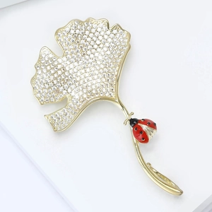 Macro-detail van de ginkgobladbroche met zirkonia pavé en rode emaille lieveheersbeestje