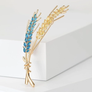 Detail of elegant wheat ear brooch with blue and yellow gems on gold finish