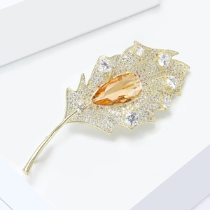 Close-up of golden leaf brooch with amber pear-shaped gemstone and white zircons